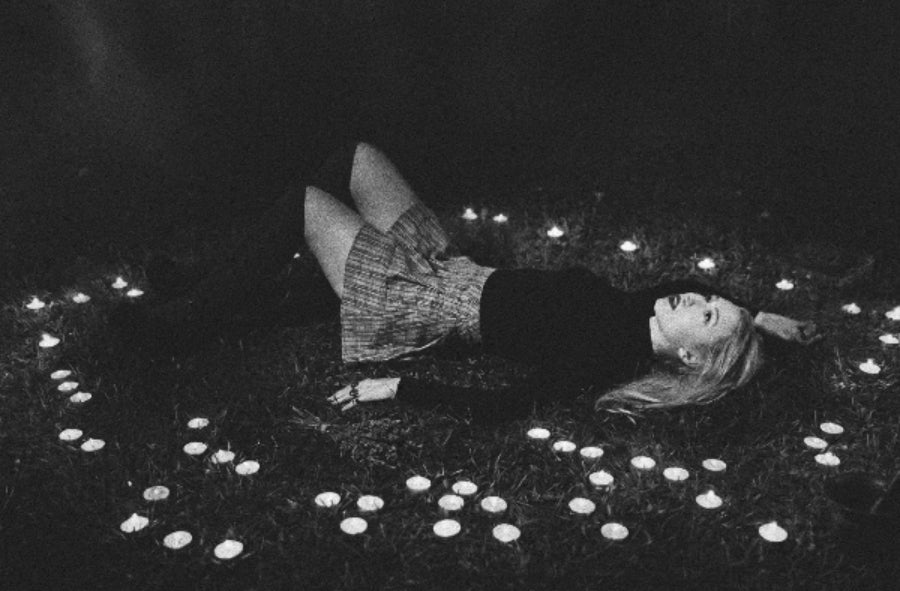 Elisabeth lying on the grass surrounded by candles in a dark setting